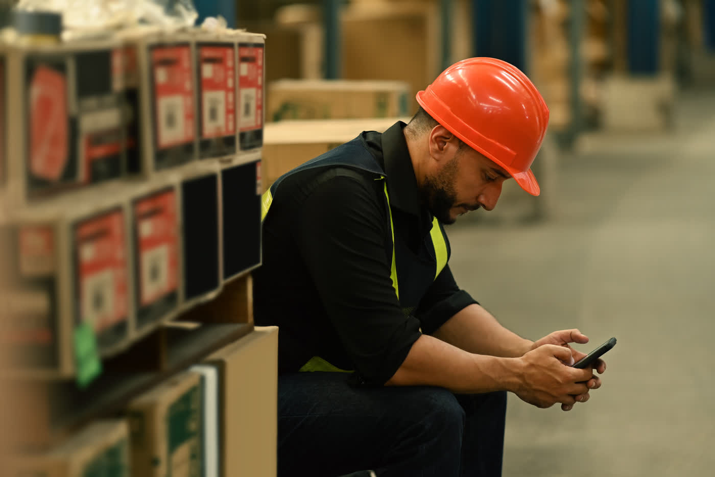 A warehouse worker in a safety-orange hard hat reading his phone